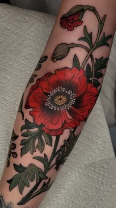 a woman's arm with a red flower tattoo on the left forearm and an orange flower in the center