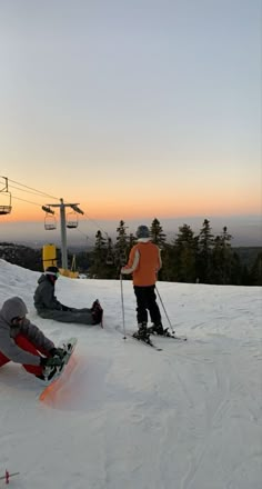 skiers and snowboarders at the top of a ski slope with sunset in background