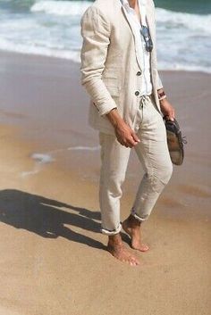 a man is standing on the beach wearing a white suit and hat with his hands in his pockets