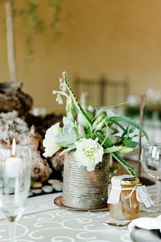 the table is set with silverware and white flowers in a tin can on it