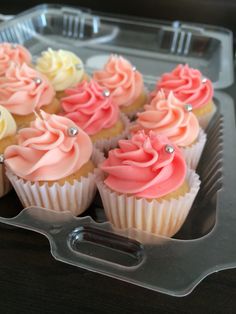 cupcakes with pink and yellow frosting sitting in a plastic tray on a table