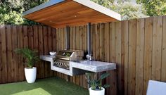 an outdoor kitchen with a grill, sink and potted plants on the grass outside