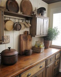 an old fashioned kitchen with wooden cabinets and pans on the wall, pots and pans hanging above