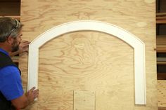 a man standing in front of a wooden wall with an arched window on it's side