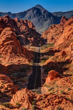 an empty road in the middle of some red rocks with mountains in the back ground