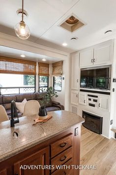 a kitchen and living room in an rv with white cabinets, wood flooring and large windows