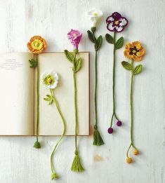 three crocheted flowers are placed next to an open book on a white surface