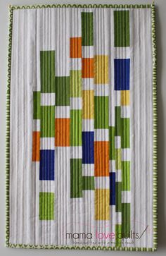 a quilted wall hanging on the side of a white wall with green, orange and blue squares