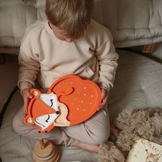 a little boy sitting on the floor holding an orange and white fox shaped bib