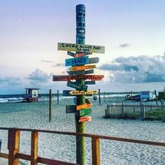 a sign post on the beach with many signs pointing to different locations and places around it