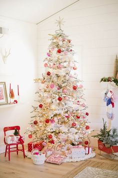 a white christmas tree with red and pink ornaments on it's branches in a living room