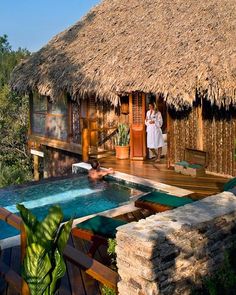 an outdoor hot tub in front of a thatched hut with a woman standing on it