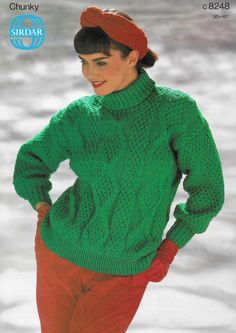 a woman wearing a green sweater and red pants with her hands on her hips while standing in the snow