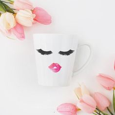 a white coffee cup with pink flowers and eyelashes on it next to tulips