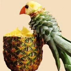 a bird sitting on top of a pineapple next to a glass filled with juice