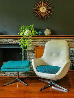 a chair and ottoman in front of a fireplace with a clock on the wall above it