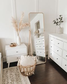 a bedroom with white furniture and a large mirror on the wall next to dressers