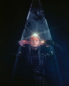 a woman standing in front of a pyramid with her hands on top of her head