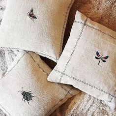 three pillows with embroidered bugs on them are sitting on a furnishing area next to a pillow