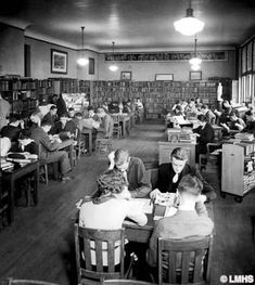 an old black and white photo of people sitting at desks in a library with bookshelves