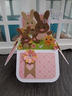 an easter card with two rabbits and chicks in a pink box on a table next to a window