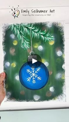 someone is holding up a christmas ornament with snowflakes and pine branches