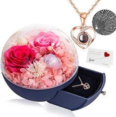 a box with flowers and a necklace in it next to a heart shaped pendant on a chain