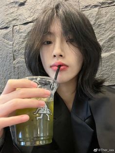 a woman drinking from a cup with a straw in her mouth while wearing a black jacket