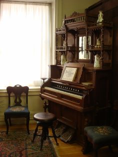 an old piano sitting in front of a window next to two chairs and a table