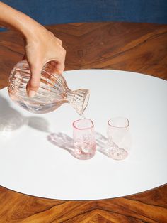 a person pours water into three glasses on a white plate with wood grained surface