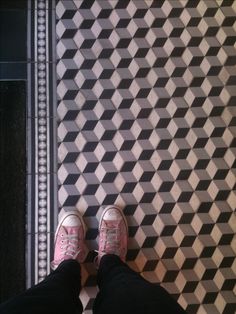 someone wearing pink shoes standing in front of a black and white tile floor with geometric designs