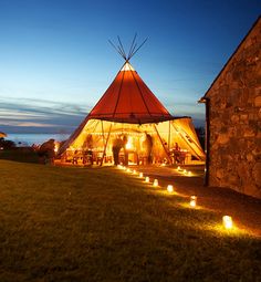 a tipi tent lit up at night with candles in the grass