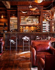 a bar with leather chairs and deer antlers hanging from the ceiling in front of it