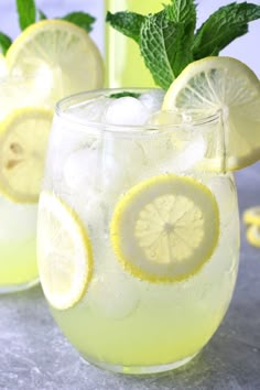 two glasses filled with lemonade and ice sitting on top of a gray countertop