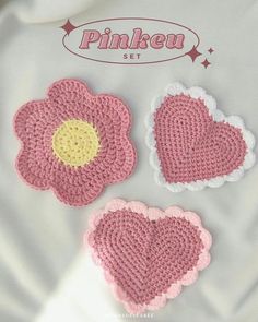 three crocheted hearts are shown on a white sheet with pink and yellow accents