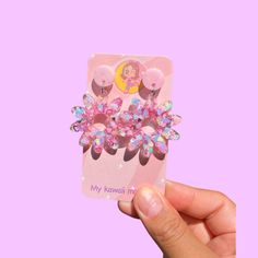 a hand holding up a pink phone case with flowers on it and a princess hair clip attached to the back