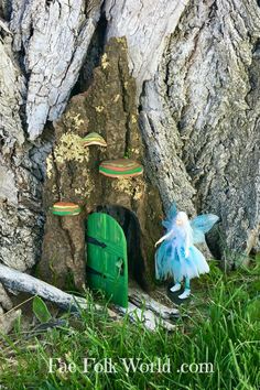 a green fairy door in the bark of a tree with a small tinkerbell doll next to it