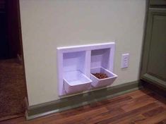 a cat is eating out of its food dish on the wall next to it's litter box