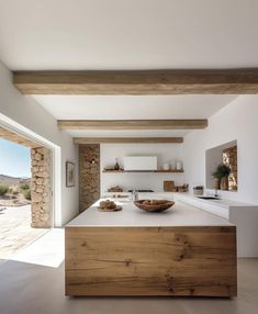 a large kitchen with an island counter top and wooden beams on the ceiling, in front of a stone wall