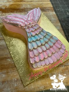 a cake shaped like a mermaid tail on top of a gold plate with pink and blue icing