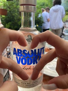 two people making a heart with their hands while holding a vodka bottle in front of them