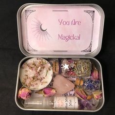 an open tin with various items inside on a black tableclothed surface and the words you're magickal written in pink