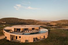 an aerial view of a circular house in the middle of a grassy area with mountains behind it