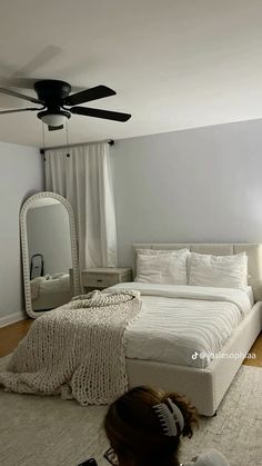 a woman sitting on the floor in front of a bed with white sheets and pillows