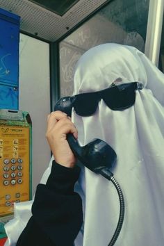 a person in a ghost costume is talking on the phone while wearing sunglasses and a headscarf