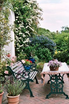 two wooden benches sitting next to each other on a brick patio surrounded by potted plants