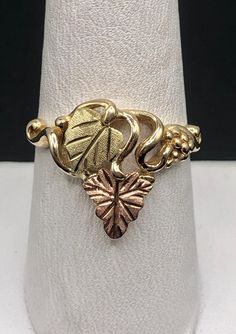 This is a lovely 10K Black Hills Gold ring with ubiquitous grape and leaf design. Ring features yellow gold grape clusters and leaves of pink and green gold. Head of ring measures 16.4mm (5/8"), band measures approximately 2.1mm at its narrowest. Stamped 10K with an indeterminate hallmark. SIZE 9 WEIGHT 4.0 grams FREE SHIPPING! Rose's Collectibles is a family-owned business with locations in Stillwater, MN and Lindstrom, MN. Visit us at rosescollectibles.com Black Hills Gold Rings, Black Hills Gold Jewelry, Black Hills Gold, Leaf Motif, Disney Jewelry, Black Hills, Still Water, Green Gold, Leaf Design