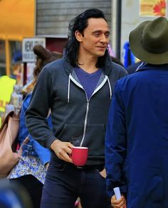 a man with long black hair is holding a red cup and talking to another man