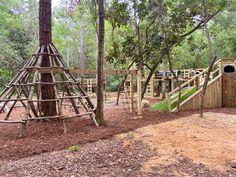 an outdoor play area in the woods with wooden structures and climbing bars for children to climb on