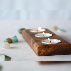 three tealight candles sitting on top of a wooden block with marbles around it